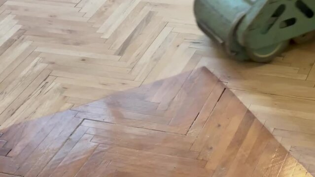 A worker is applying a scraper polish to a parquet that has deteriorated.