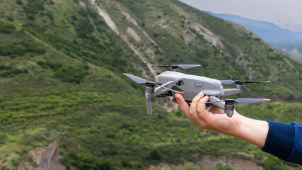 Hand of a young man holding a drone before flight with mountain background, selective focus