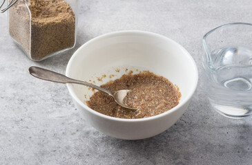 A bowl with ground flax and water, a jar of ground flax and a jug of water on a gray textured background. Cooking a vegan flax egg - 617809217
