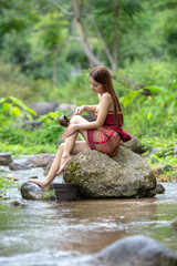 Beautiful Woman asia slim fitness model posing sexy in creeks wearing Sarong shower and wash a clothes in the stream from the waterfall to show the lifestyle of people in the countryside with nature
