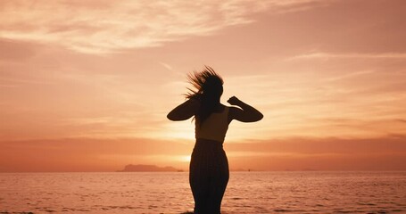 Silhouette of happy woman jumping on the beach enjoying tropical sunset during summer vacation. Concept of happiness and bliss where people are jumping for joy celebrating.