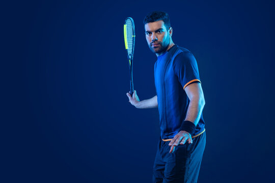 Squash player on a squash court with racket. Man athlete with racket on court with neon colors. Sport concept. Download a high quality photo for the design of a sports app or betting site.