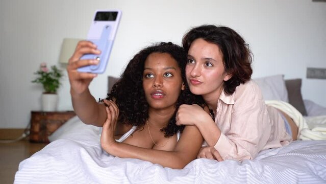 Smiling young diverse girlfriends taking selfie with smartphone in daylight