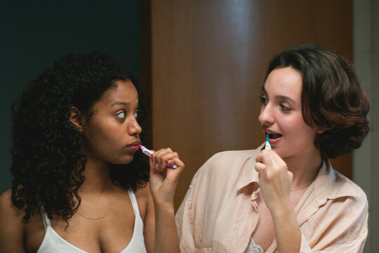 Young diverse women standing and brushing teeth together
