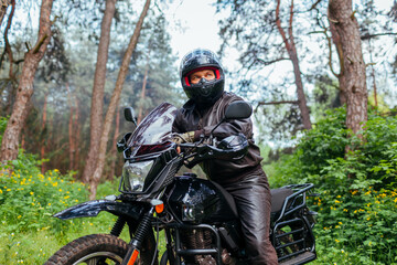 Fototapeta na wymiar Senior motorcyclist riding motobike outdoors. Man in leather jacket resting after ride in summer forest. Space