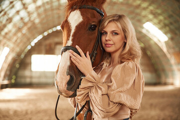 Portrait of beautiful young woman that is with horse indoors