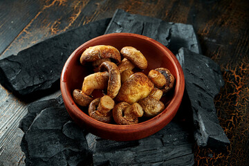 Mushrooms grilled on charcoal in a bowl on a dark background
