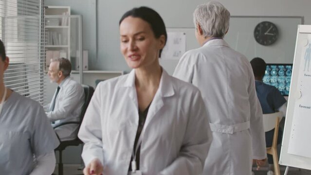 Medium shot of two multiethnic female doctors in white lab coats shaking hands after having conversation at workplace