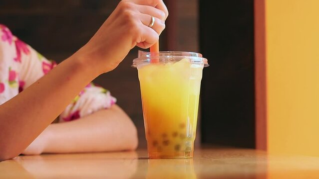 Bubble tea. A drink in a plastic cup in the hands of a girl. Stir the bubble tea with a straw. Woman drinking of Taiwan Bubble tea