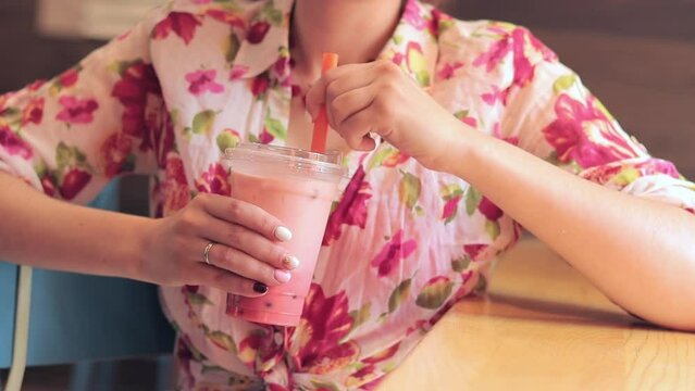 Bubble tea. A drink in a plastic cup in the hands of a girl. Stir the bubble tea with a straw. Woman drinking of Taiwan Bubble milk tea