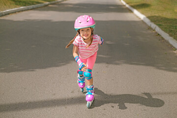 A child in sports protective gear and a helmet rushes along an asphalt track on roller skates at...