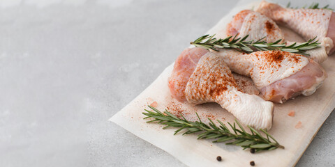 Raw chicken legs with spices and rosemary sprigs on a wooden cutting board. Copy space