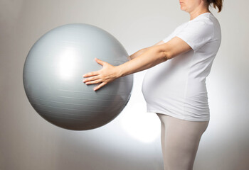 Fototapeta premium Pregnant girl with a fitball on a white background. The concept of doing sports and fitness during pregnancy. Health and pregnancy.