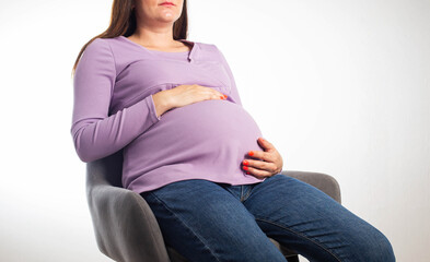Pregnant girl sits on a chair at the workplace, white background. The concept of maternity leave and working conditions under the law. Benefits and maternity leave. Copy space for text