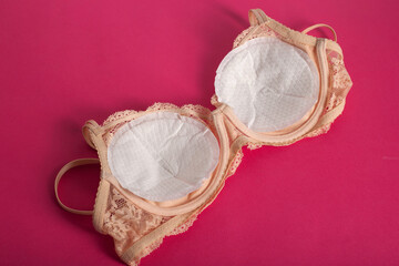 Women's bra with liners against the flow of milk from the breast of a nursing woman on a pink background. Copy space for text