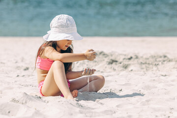 Side view cute little girl playing in the sand on a sunny beach. Summer vacation concept