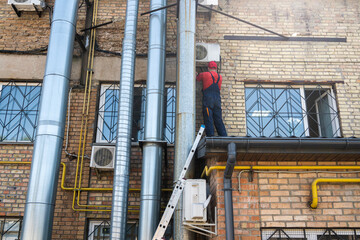 A master on the roof repairs the air conditioner. The master repairs the wires of the Internet on the roof