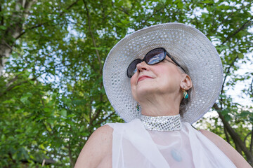 Portrait of a happy elderly woman 65 - 70 years old in a straw hat on the background of nature, closeup