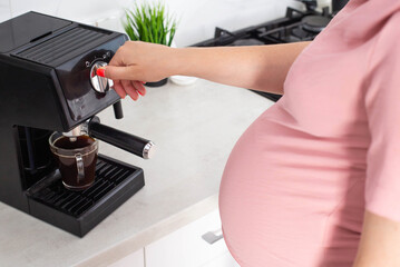 A pregnant woman prepares coffee in a coffee machine. Coffee and pregnancy, close-up. The benefits...