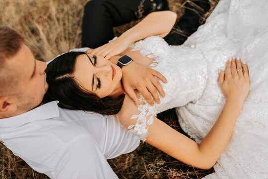 The bride and groom are lying on the dry grass and hugging, a woman in a white wedding dress. Beautiful autumn wedding photo.