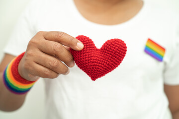 Asian lady wearing rainbow flag wristbands and hold heart, symbol of LGBT pride month celebrate annual in June social of gay, lesbian, bisexual, transgender, human rights.