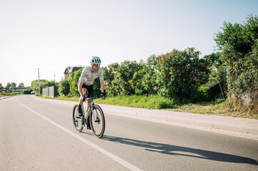 Obraz premium Cyclist athlete trains outside the city on a bicycle and rides fast on the road. Recreation.
