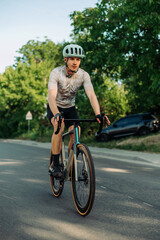 Fototapeta premium Photo of a handsome male cyclist in sports gear on a road bike training on an asphalt road outside the city, looking away.