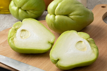 Whole and halved fresh chayote on a cutting board close up