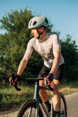 Portrait of a handsome male cyclist in gear riding a road bike outside the city at sunset.