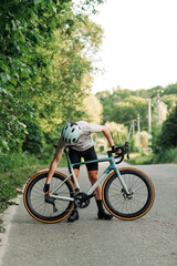 Sporty young man in gear checks the bike before starting training on the asphalt road outside the city.