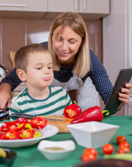 mother and  son preparing food in the kitchen. mother showing recipe on tablet