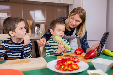 mother and two sons preparing food in the kitchen. mother showing recipe on tablet