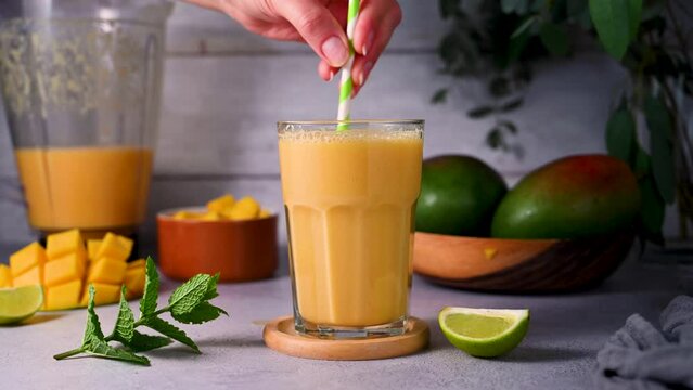 Mixing mango smoothie in a glass with fresh mango, mint and lime.