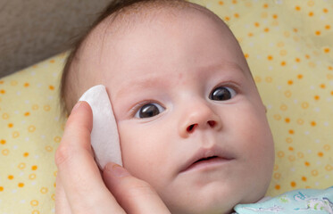 The mother washes the child's eyes with a cotton pad. Eye care and hygiene for newborns.