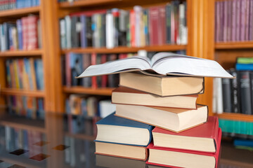 Many books stacked on a glass table and library in the background with many copies.