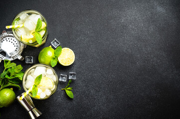 Mojito with rum, lime, mint and ice on black background with bar utensils. Flat lay with copy space.