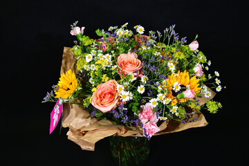 Beautiful colorful bouquet with roses and sunflowers among meadow flowers. Focused on the center of the image.