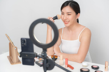 An Asian beauty blogger uses a blush brush to brush on her face during a live online makeup tutorial via the Internet.