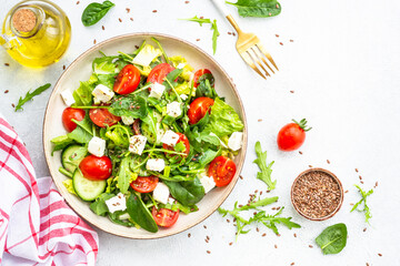 Spring salad in craft plate. Spinach, arugula, tomatoes and feta with olive oil. Top view on white.