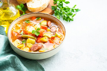 Minestrone soup, italian vegetable soup with smoked sausages, Top view on white table.