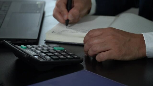 Businessman working with calculator taking notes in notebook
