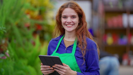 Portrait of a female florist employee staff holding tablet standing inside Plant Store smiling at camera