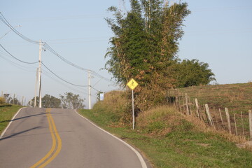 Linda estrada asfaltada com placa de sinalização para ciclista no local.