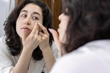 portrait of a woman's reflection in the bathroom mirror at home removing pimples from her face....