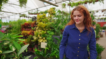 Joyful Woman Picking Plant from Shelf, Strolling Through Horticulture Gardening Supply Store Aisle