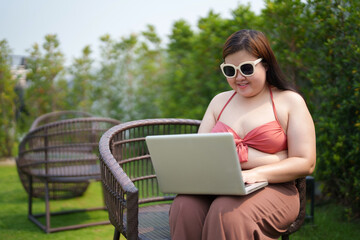 Beautiful plus size, Portrait of Confident asian woman sitting at poolside using laptop..