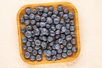 A few ripe blueberries with a bamboo tray on a linen cloth, macro, top view.