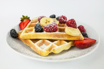 Square Belgian waffles with berries and jam on a light white background.