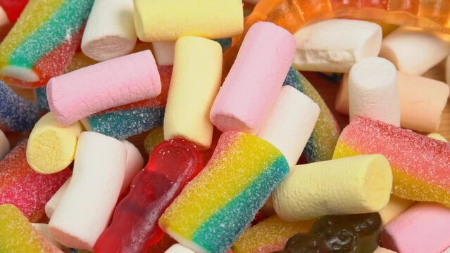 Multi colored gummy jelly sweets rotating on wooden board. Multicolored gummy candy jelly confectionery, made with sugar and gelatin or marshmallow