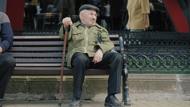 An old man sits on a bench in the park. Portrait of a pensioner on the background of the city
